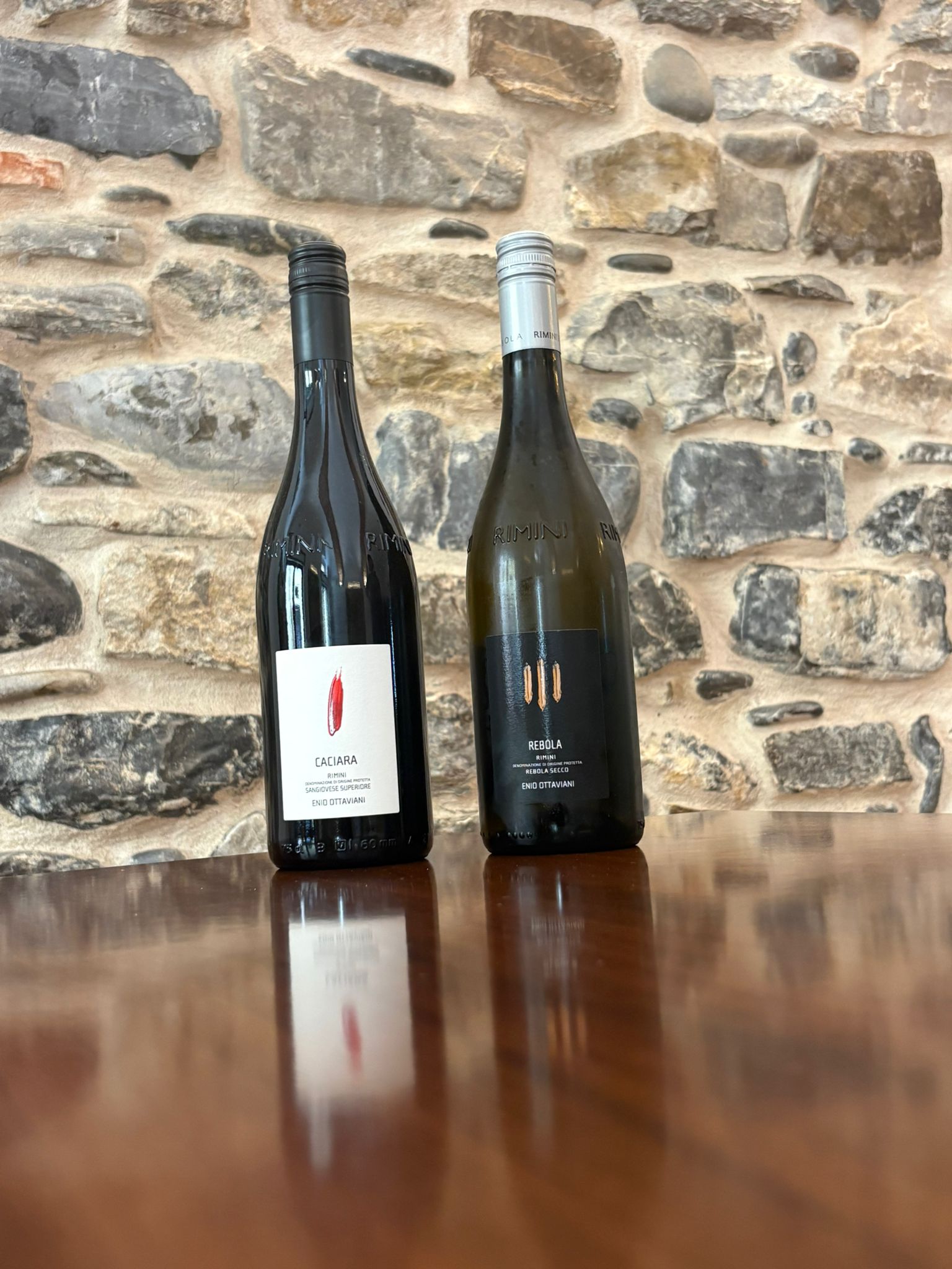 Due bottiglie di vino su un tavolo davanti a una parete in pietra